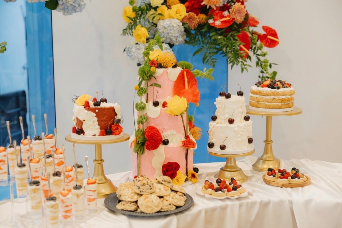 A Cardinal Cake Co. dessert table with tiered floral cakes, cookies, fruit tarts and dessert cups